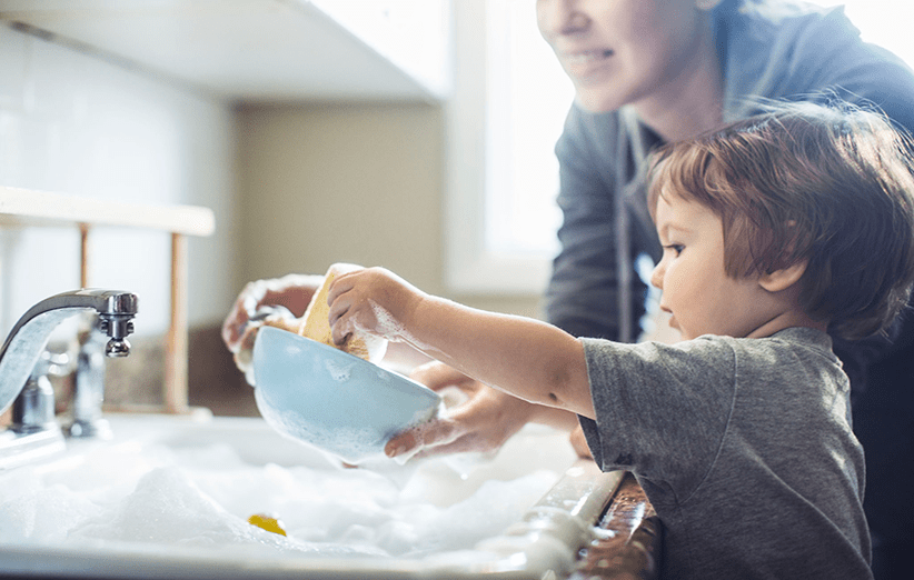 کودکی در شستن ظروف کمک می‌کند.